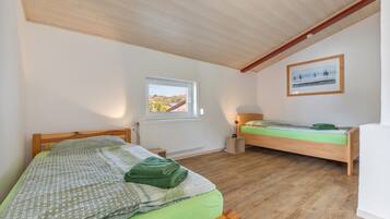 Quarto com duas camas de madeira, janela com vista, radiador e quadro pendurado na parede.