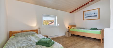 A bedroom with two wooden beds, a window with a view, a radiator, and a framed picture on the wall.