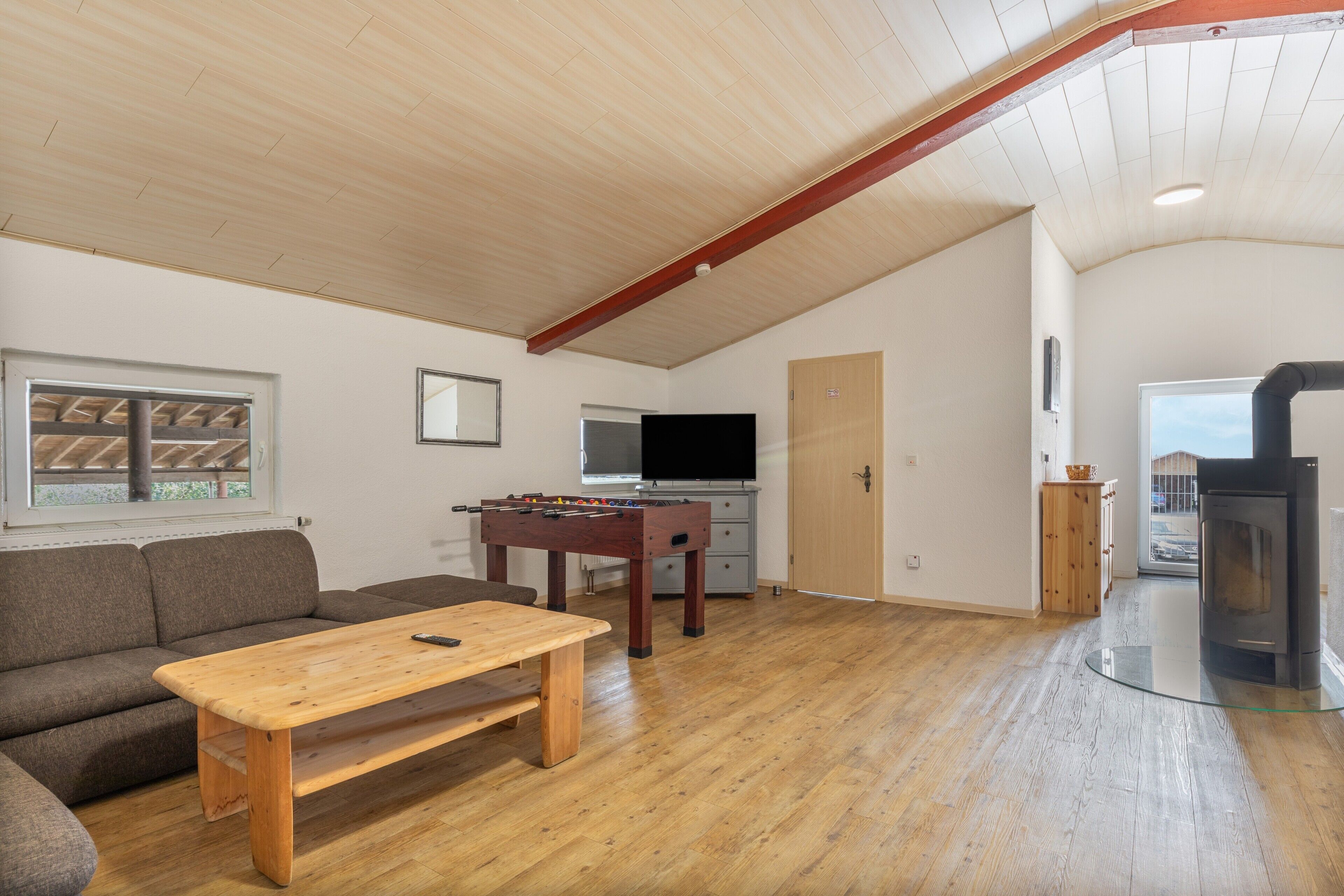 A cozy living room with a wooden table, sofa, and a foosball table.