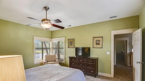 A bedroom with a bed, a ceiling fan, a dresser, a television, and a window with blinds. - My Magnolia @ Magnolia Bay (Miramar Beach)