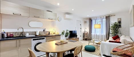 A modern kitchen with a dining area, a living room with a sofa and a TV, and a bathroom with a shower.