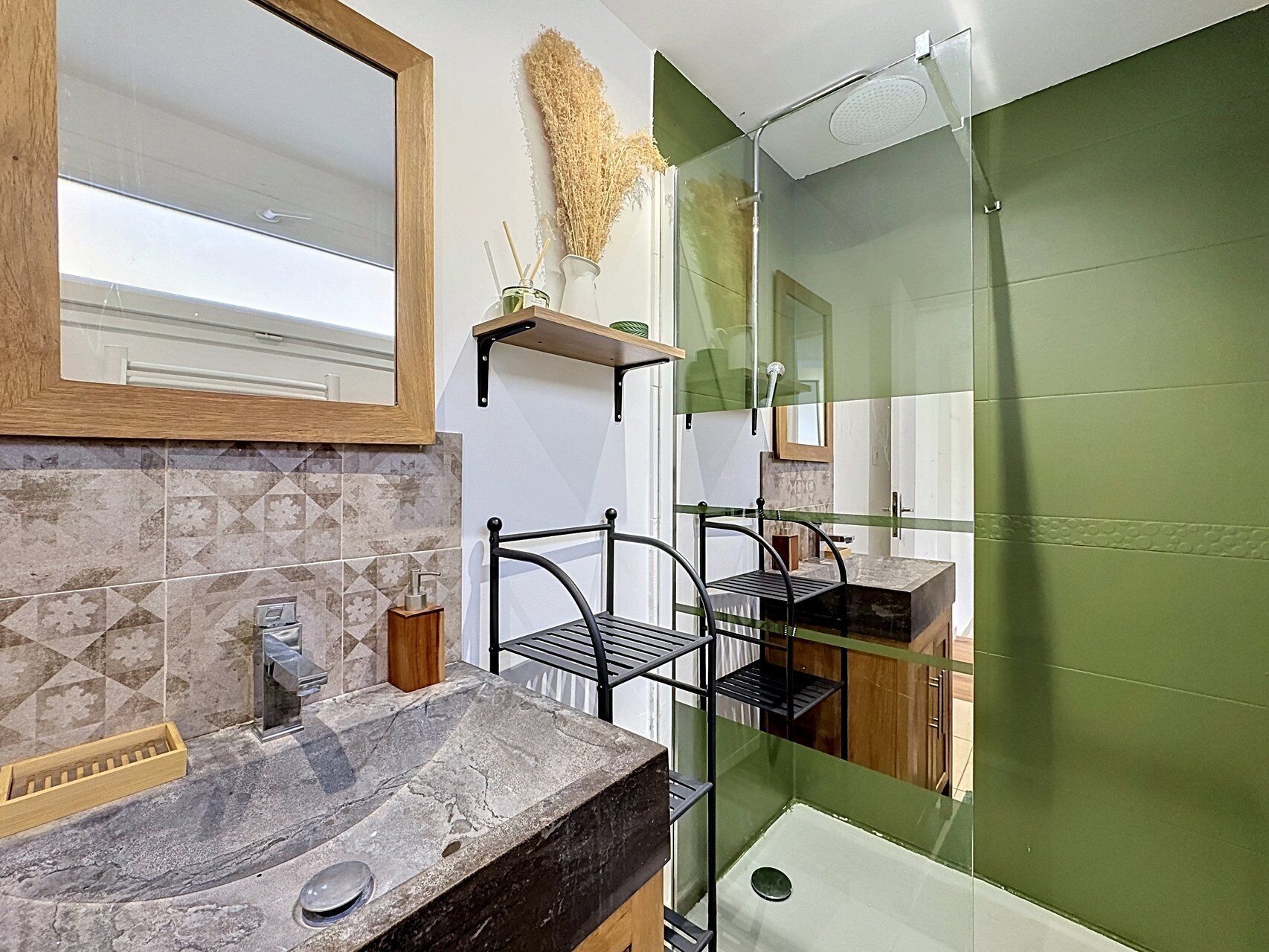 A modern bathroom with a marble sink, a glass shower enclosure, and a green accent wall.