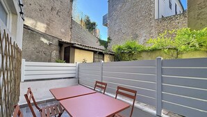 Un pati amb una taula i caires, una tanca blanca i un edifici amb parets de pedra.
