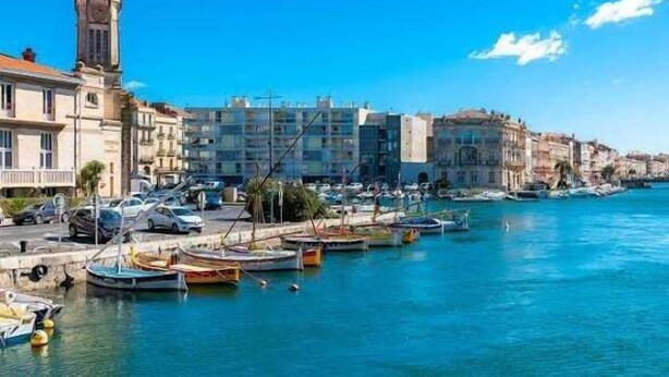 Un poble costaner amb una torre destacada, una marina plena de vaixells i una combinació d'edificis històrics i moderns.