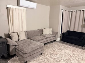 A living room with a grey sectional sofa, a black sofa, and a patterned rug.