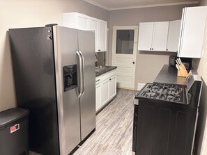 A kitchen with a stainless steel refrigerator, white cabinets, a black stove, and a trash bin.