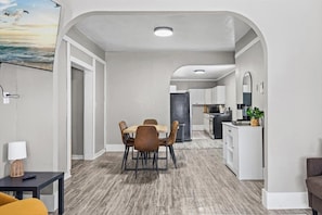 A modern interior with a dining area, kitchen, and living space, featuring a wooden floor, white walls, and a view of the sea.