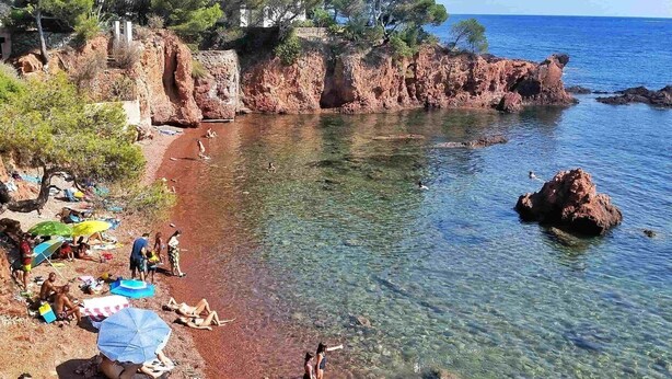 En strand med klart vatten, klippiga branter och folk som solar.