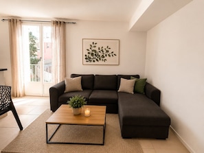 Ein Wohnzimmer mit einer Eckcouch, einem Couchtisch mit Pflanze, einem gerahmten Kunstwerk an der Wand und Blick durch eine Glastür.