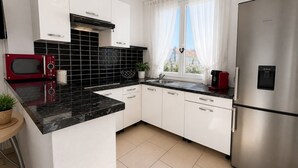 Ett modernt kök med vita skåp, ett svart kaklat stänkskydd, ett kylskåp i rostfritt stål och en röd mikrovågsugn.