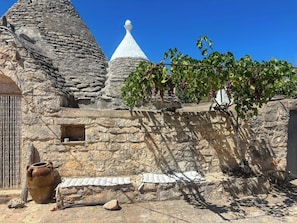 Ein Steinhaus mit einem Kegeldach, einer Weinrebe mit Trauben und einem großen Topf.