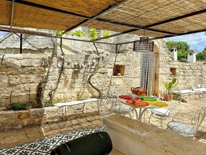 A stone-walled outdoor area with a table set for dining, metal chairs, and a covered seating area. - 17th-century trullo with private pool (Ostuni)