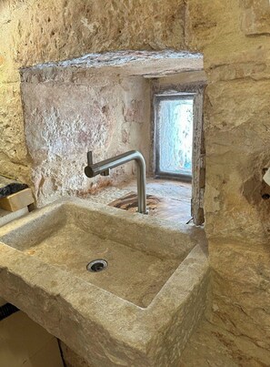 A stone sink with a modern faucet in a rustic room with exposed stone walls and a small window. - 17th-century trullo with private pool (Ostuni)