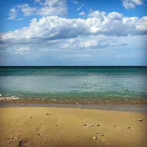 Ein Strand mit klarem Wasser, einem sandigen Ufer und einem teils bewölkten Himmel.