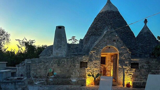 A stone building with a pool in front, stone chairs, and a warm light inside. - 17th-century trullo with private pool (Ostuni)