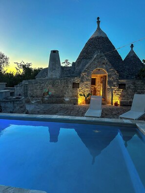 A stone building with a pool in front, stone chairs, and a warm light inside. - 17th-century trullo with private pool (Ostuni)