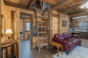 Ein Holzblockhaus-Interieur mit einer Holztreppe, einem roten Ledersofa, einem kleinen Tisch und einer Küchenzeile.