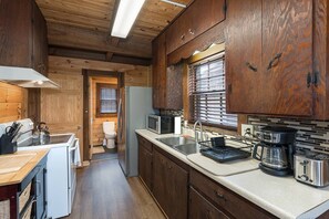 Eine kleine Küche mit Holzschränken, einem Kühlschrank, einer Mikrowelle, einer Kaffeemaschine und einem Toaster.