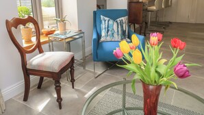 A living room with a blue sofa, a wooden chair, a glass coffee table, and a vase with tulips. - The Cottage (Swindon)