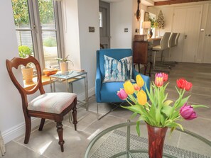 Ein Wohnzimmer mit einem blauen Sofa, einem Holzstuhl, einem Glastisch und einer Vase mit Tulpen.