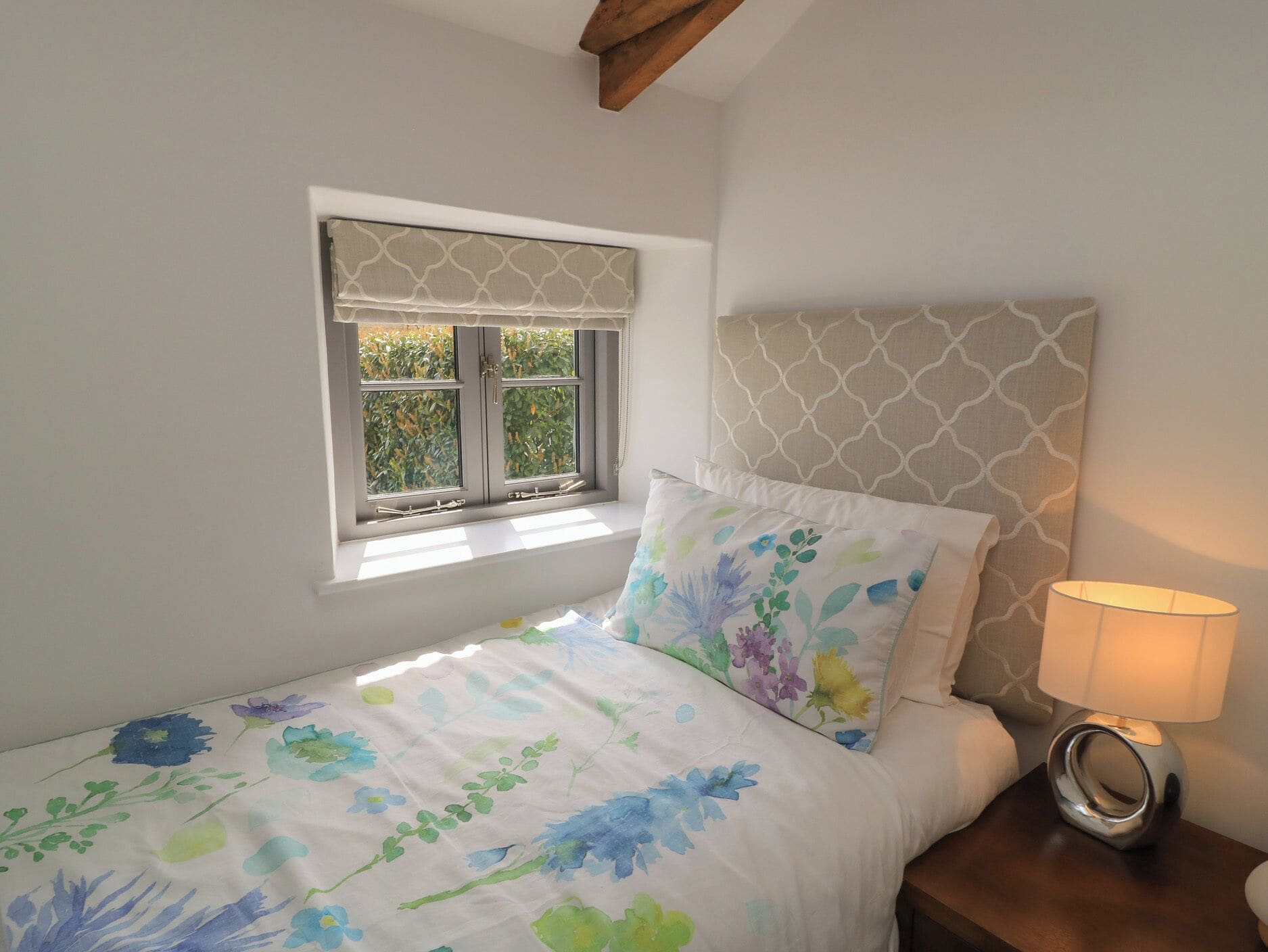A bedroom with a bed, a window with a view, a bedside lamp, and a headboard.