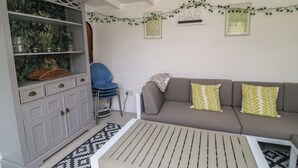 A room with a grey sofa, a white cabinet with drawers, a patterned rug, and a ceiling fan. - The Cottage (Swindon)