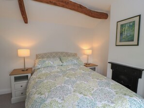 Ein Schlafzimmer mit einem Bett, zwei Nachttischen mit Lampen, einem Schminktisch und einem Kamin. An der Wand hängt ein gerahmtes Bild.