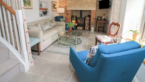 A living room with a sofa, a blue armchair, a glass coffee table, and a fireplace. - The Cottage (Swindon)