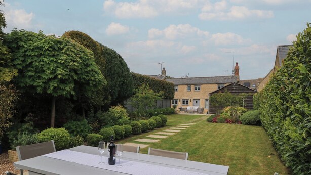 A patio with a table and chairs, a lawn, and a house in the background. - The Cottage (Swindon)