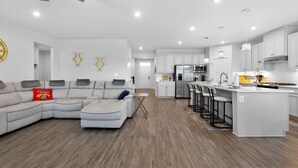 Uma sala de estar moderna com um sofá seccional, uma cozinha com armários brancos e um espaço bar.