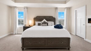 Quarto com cama grande, mesa de cabeceira, ventoinha no teto e janela com cortinas.
