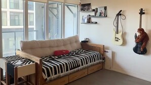 Ein Zimmer mit einer Couch, einem Schreibtisch und einem Fenster. An der Wand hängen Gitarren.