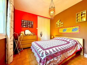 Un dormitorio con cama, cómoda, puerta y pared con estante y cuadro.
