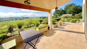 Eine überdachte Terrasse mit Tisch und Bank, eine Hängelampe und Blick auf einen Weinberg.