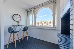 A balcony with two black chairs, a small table, a potted plant, and a wall clock.