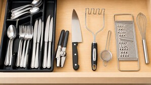 Un cajón con diversos utensilios de cocina, como cucharas, tenedores, cuchillos, un rallador, un colador y un batidor.
