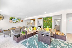A modern living room with a sofa, dining table, chairs, and a kitchen area visible through an open door. - Walk to Siesta Key Beach & Village | Pool | Dock | Game Room! (Siesta Key)