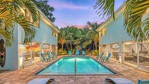 Una piscina con sillas de descanso, palmeras y un cielo al atardecer.