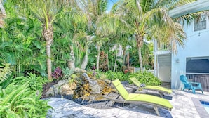 A tropical garden with a stone pathway, lounge chairs, and a small waterfall. - Walk to Siesta Key Beach & Village | Pool | Dock | Game Room! (Siesta Key)