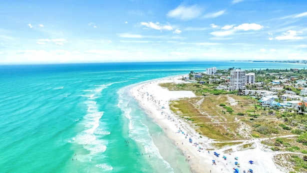 An aerial view of a beach with a long stretch of white sand, clear turquoise water, and a dense cluster of buildings in the background. - Walk to Siesta Key Beach & Village | Pool | Dock | Game Room! (Siesta Key)