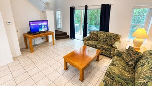 Un salon avec un canapé, une table basse, un téléviseur et un escalier.