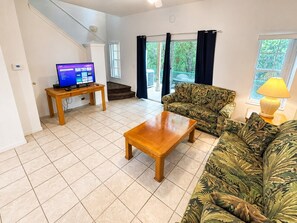 Ein Wohnzimmer mit Sofa, Couchtisch, Fernseher und Treppe.