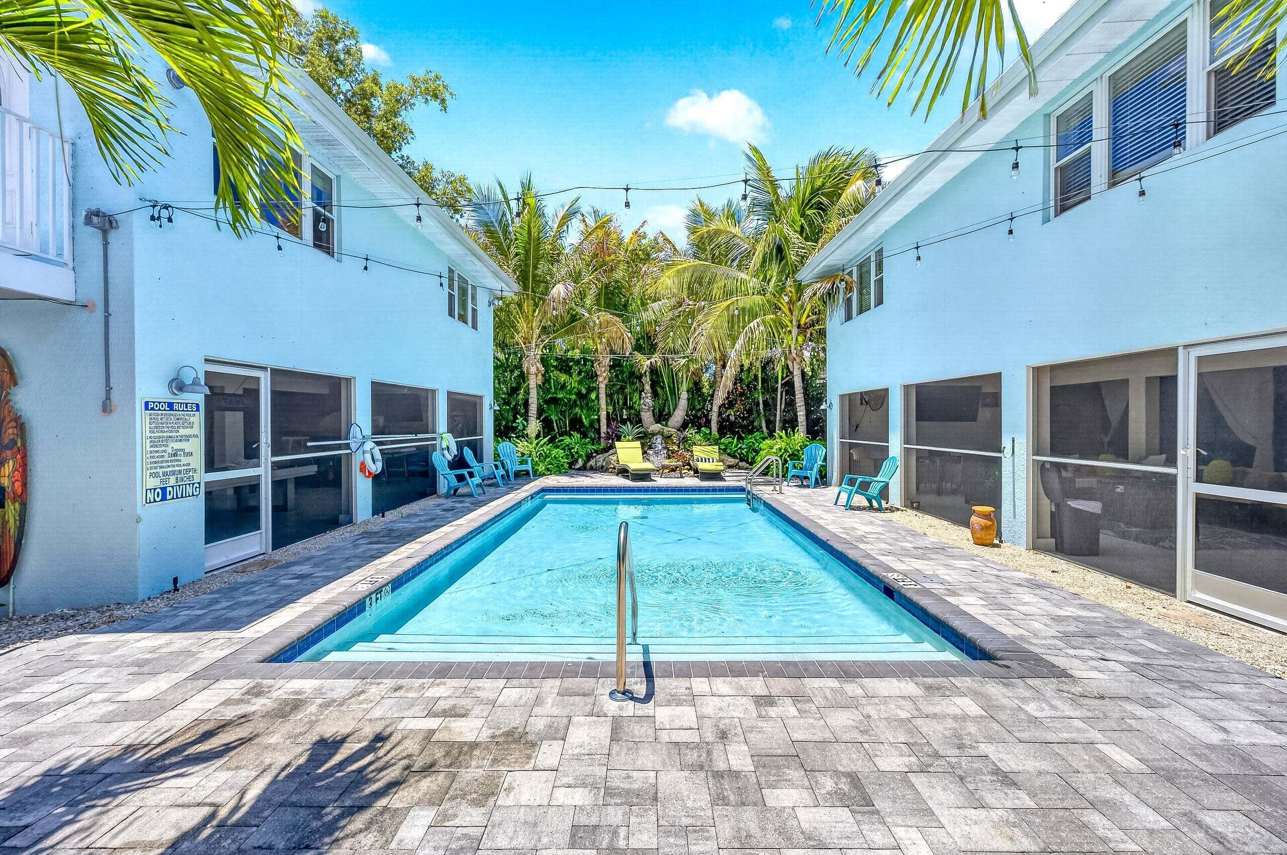 Une piscine avec un panneau indiquant les règles d’utilisation, entourée de palmiers et agrémentée de mobilier d’extérieur.