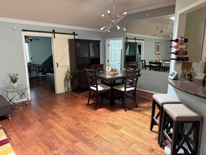 Ein Essbereich mit Holztisch und Stühlen, eine Küche mit Herd und Schränken sowie ein Wohnbereich mit Sofa und Fernseher.