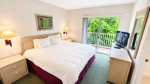 A bedroom with a bed, bedside tables, a TV, and a balcony with a view of greenery. - Family Fun Escape | Near Disney & Resort Pool (Kissimmee)