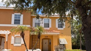 A yellow building with the number 1049, a palm tree, and a small bush in front. - Family Fun Escape | Near Disney & Resort Pool (Kissimmee)