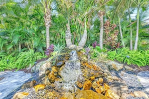 Ein Garten mit einem kleinen Wasserfall, Palmen und verschiedenen tropischen Pflanzen.