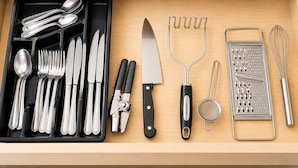 Un cajón con diversos utensilios de cocina, como cucharas, tenedores, cuchillos, un rallador, un colador y un batidor.