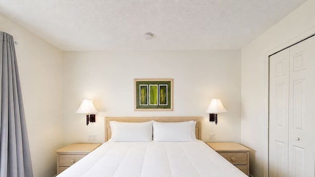 Habitación de hotel con una cama grande, dos mesitas de noche, una mesilla auxiliar, una puerta y un cuadro colgado en la pared.