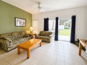 A living room with a sofa, armchair, coffee table, and a ceiling fan. - Easy family stay with resort pool (Kissimmee)
